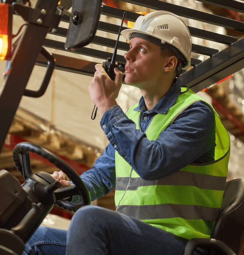Warehouse operator demonstrating how to drive a forklift safely while using a two-way radio