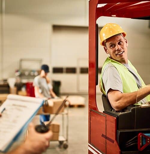 Instructor guiding a seated operator during forklift refresher training