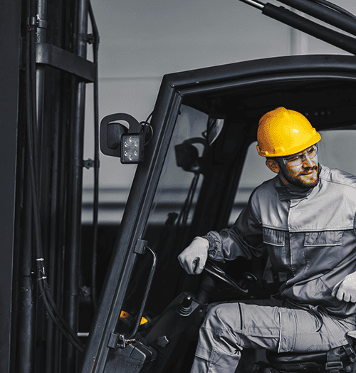 Male forklift operator wearing a yellow hard hat looking over his shoulder from the cab