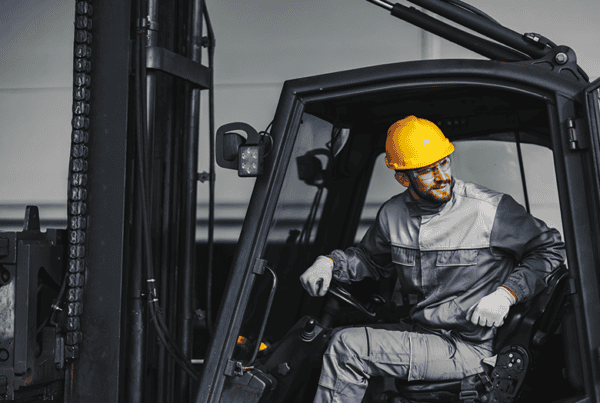 Male forklift operator wearing a yellow hard hat looking over his shoulder from the cab