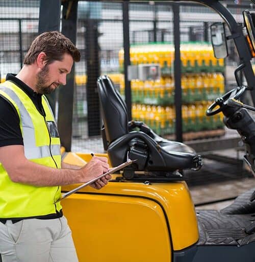Worker in a high visibility vest writing on a clipboard beside a yellow forklift