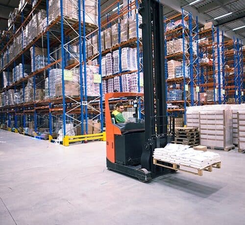 Operator using a reach truck to handle a pallet beside tall warehouse racking