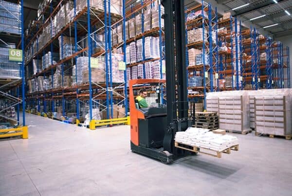 Operator using a reach truck to handle a pallet beside tall warehouse racking
